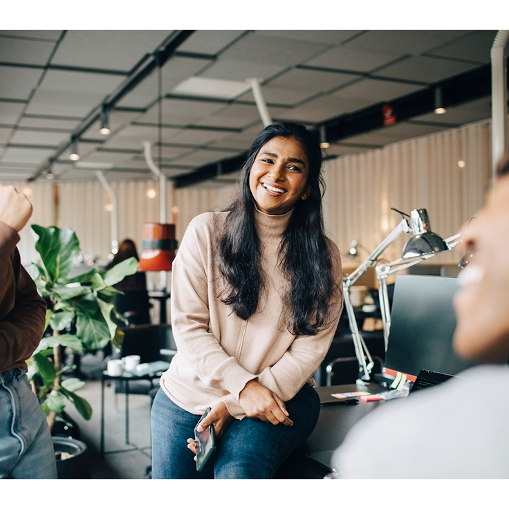 Girl smiling with colleagues, leaning against desk in office