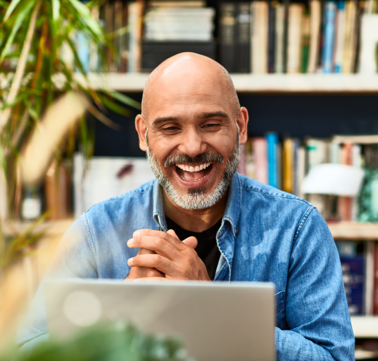 Man smiling and clasping hands, sitting at desk in library in front of computer