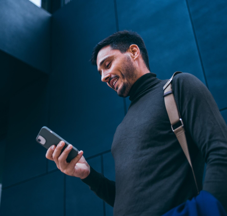 Man wearing high neck top with bag over shoulder, looking down at phone in hand