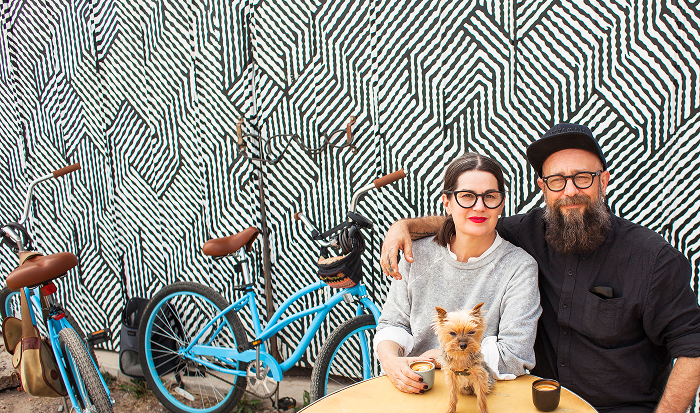Man and woman sitting at table outdoors, holding a dog on their laps
